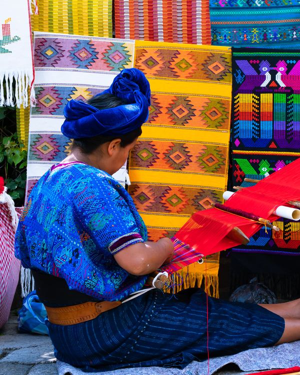 A Maya weaver at her backstrap loom, surrounded by the cloth she has made.