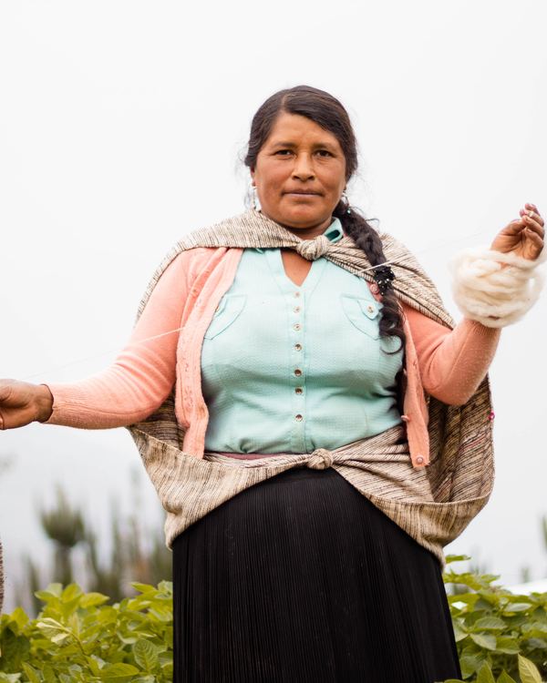 An Andean woman spinning sheep wool by hand, outdoors.