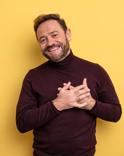 A man with both hands held over his heart, looking straight at the camera.
