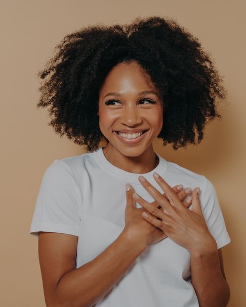 A woman with both hands resting over her heart, smiling and looking away.